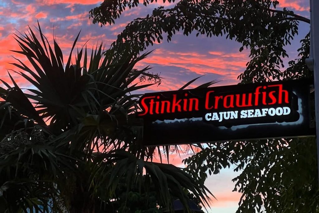 The lit Stinkin' Crawfish Cajun Seafood sign under palm trees at a pink Key West sunset