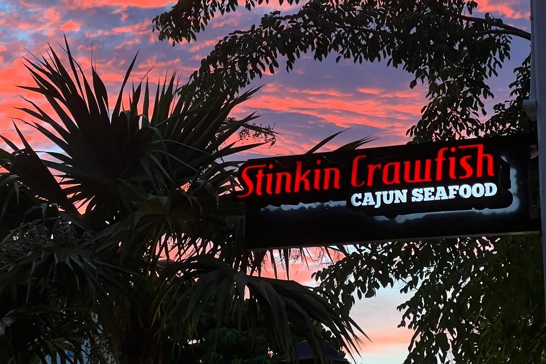 The lit Stinkin' Crawfish Cajun Seafood sign under palm trees at a pink Key West sunset
