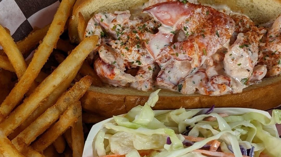 A lobster roll with fries and coleslaw in a checkered basket at Stinkin' Crawfish Key West
